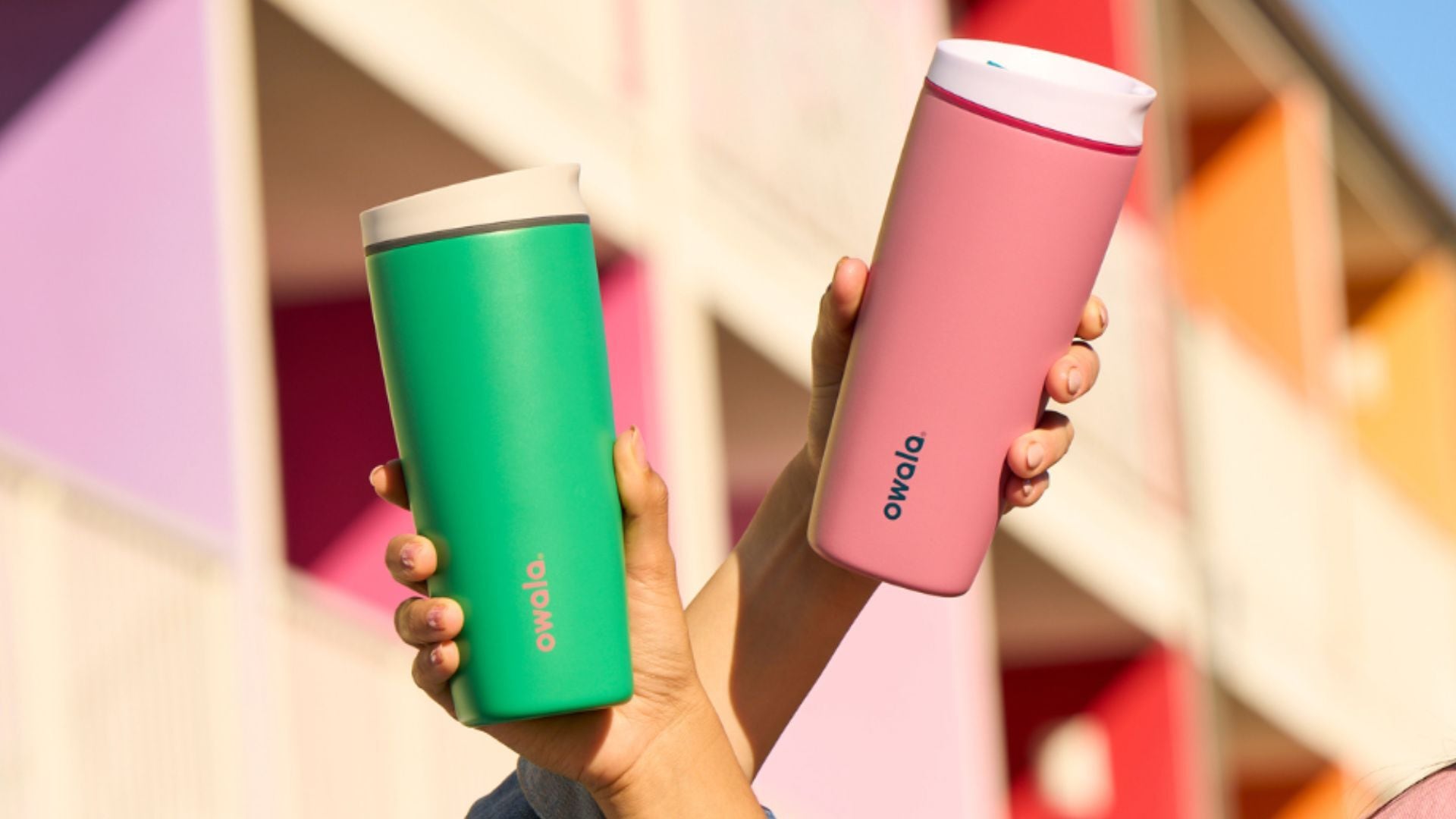 two hands holding up bright coffee tumblers