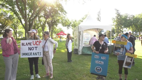 People hold signs that read "Blame UCP not immigrants" and "No to coal" at the KDays pancake breakfast at the Alberta legislature on July 16, 2026. (Sean McClune / CTV News Edmonton)