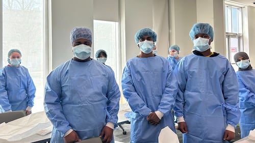 Students wear blue scrubs in a classroom.