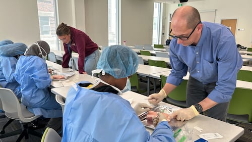 Students wear blue scrubs in a classroom.