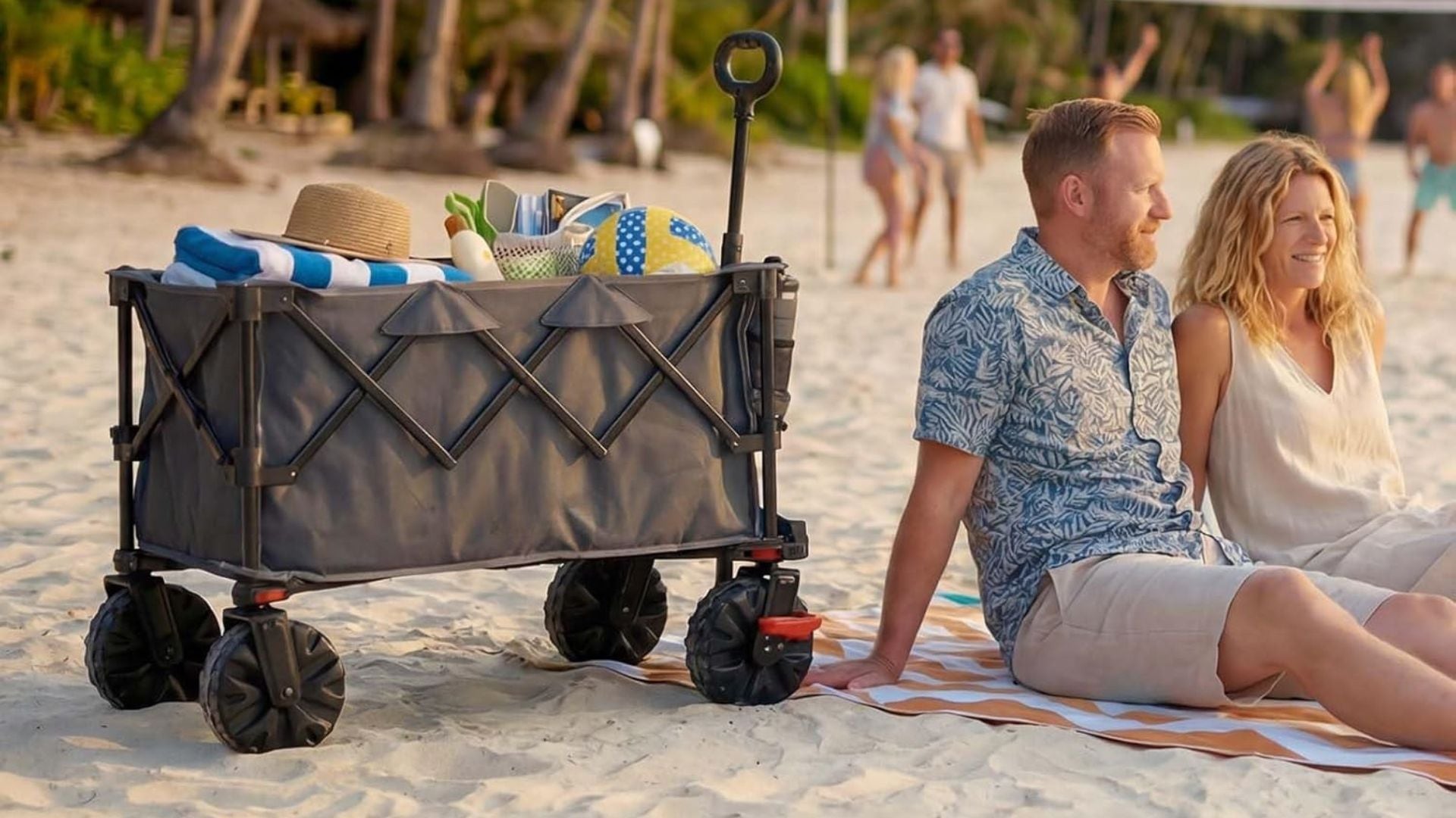 a wagon on a beach next to a pair of adults sitting on a blanket