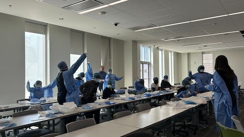 Students wear blue scrubs in a classroom.