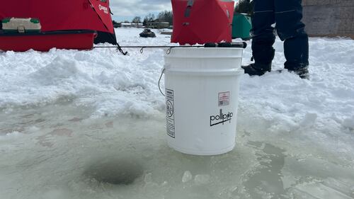 An ice fishing rod and bucket are pictured next to a hole drilled in the ice for fishing. (Avery MacRae / CTV Atlantic)