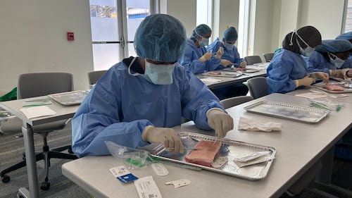 Students wear blue scrubs in a classroom.