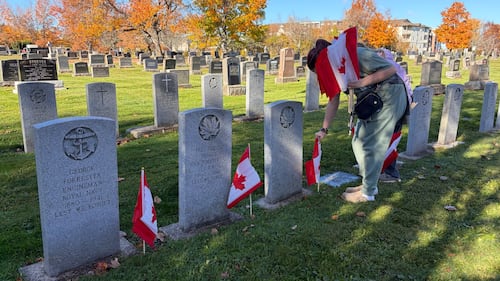 A girl places a Canadian flag on a grave.