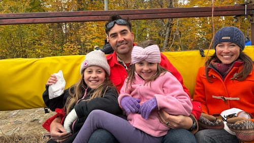 A family of four poses for a photo while riding on a tractor.