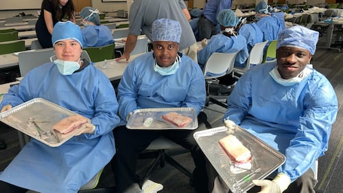 Students wear blue scrubs in a classroom.