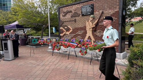 A member of the military carries a wreath past a monument.