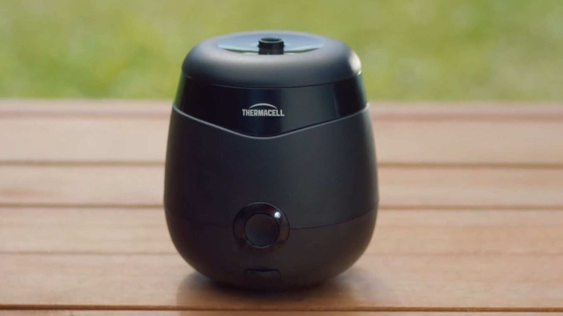 A Thermacell Mosquito Repellent Device on a wooden patio table outdoors.
