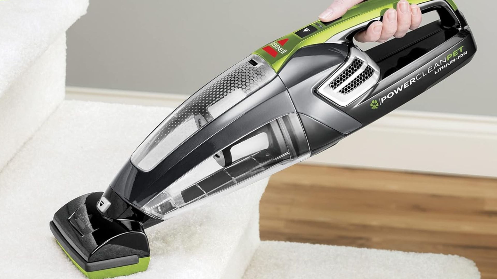 A person is cleaning carpeted stairs with a Bissell hand vacuum.