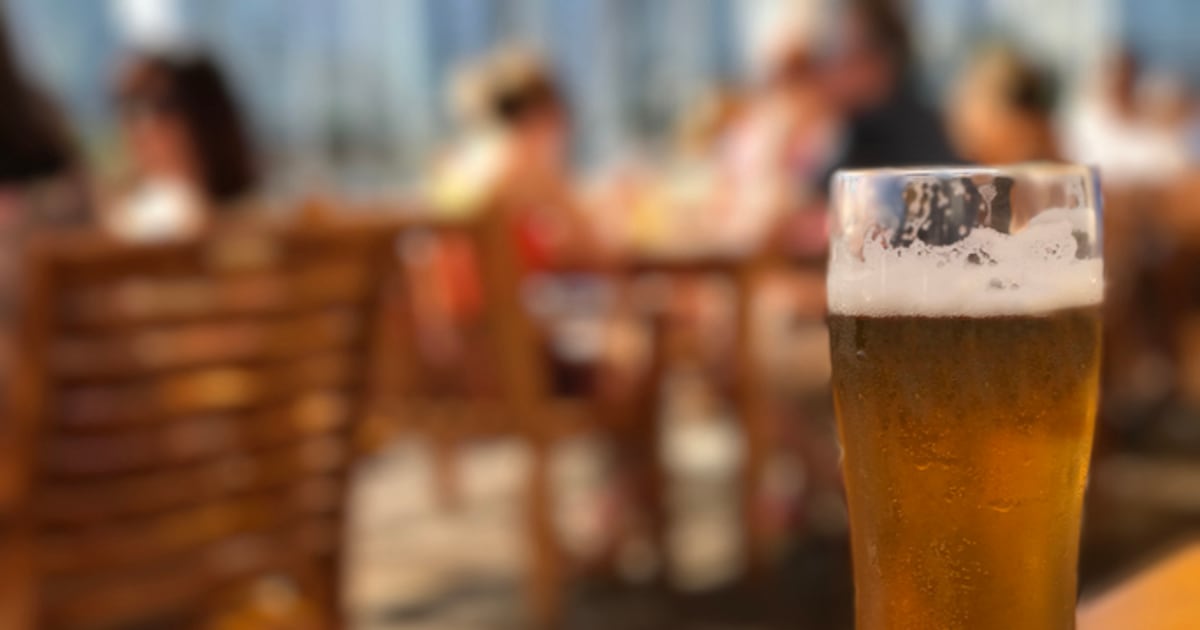 Glass of cold beer on a patio table with a blurry background of people and city