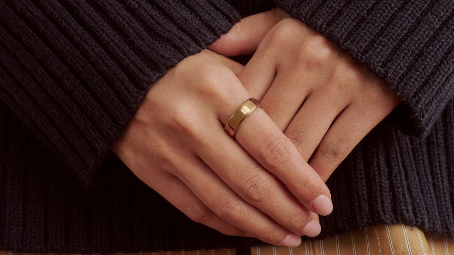 A person wearing a black sweater and an OURA Ring 5 on their pointer finger.