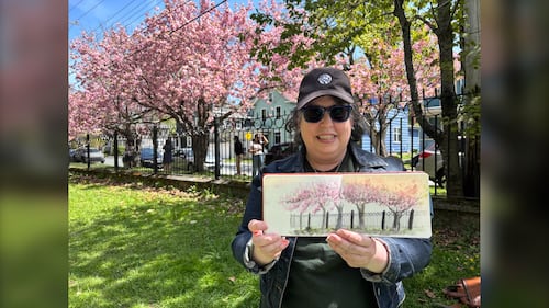 An artist poses with a painting of cherry blossoms.
