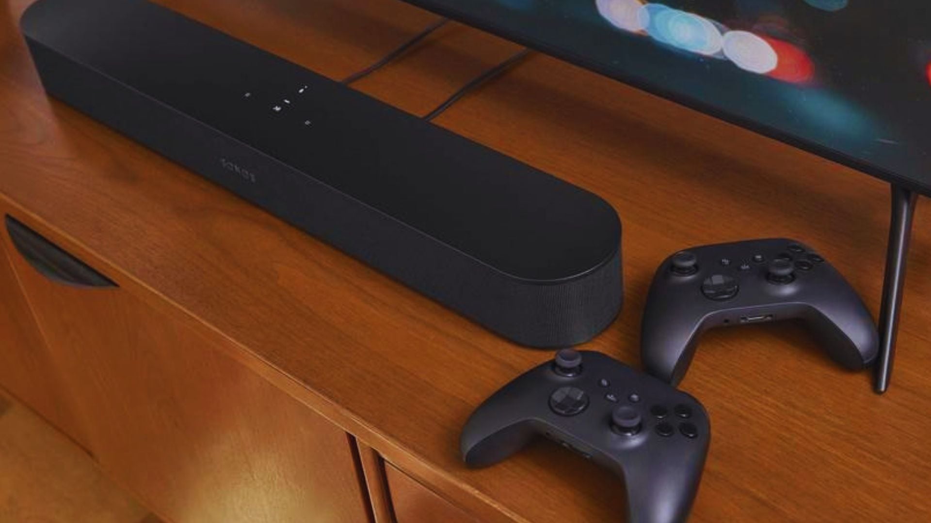A Sonos soundbar with gaming controllers beside it.